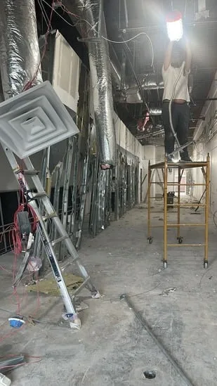 Commercial interior renovation with worker installing lighting on scaffolding.